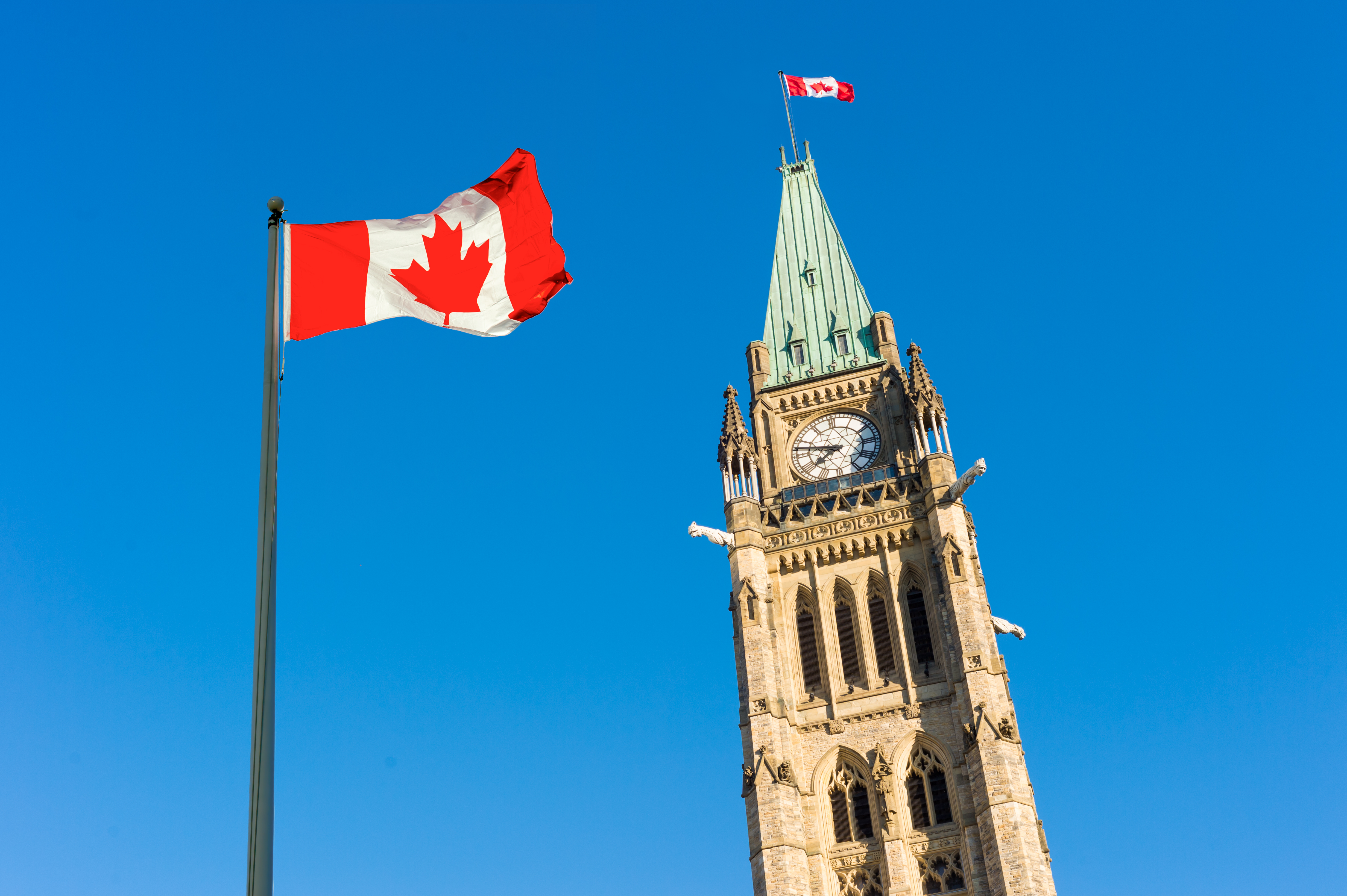 Close up of peace tower (parliament building)  with a big canadian flag over blue sky in Ottawa, Canada