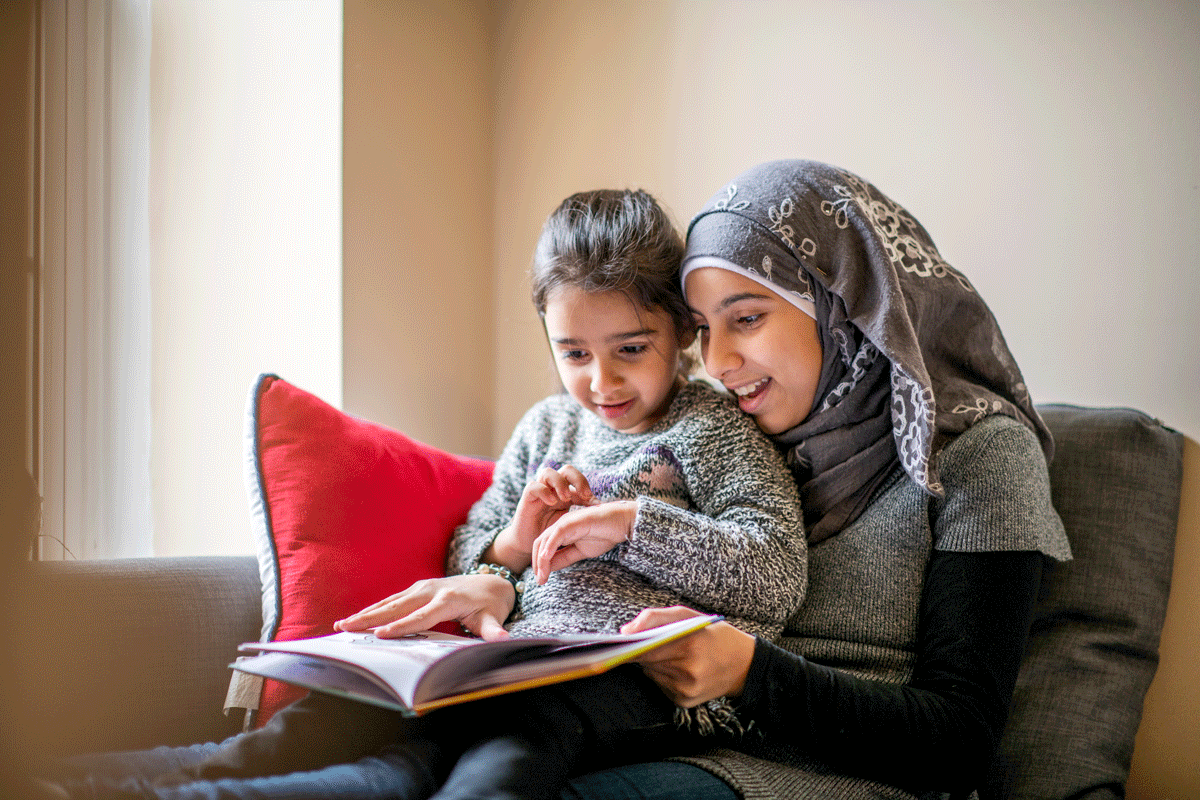 A women sitting on the sofa reading with their daughter.
