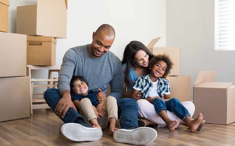 A family sitting on the floor together surrounded by moving boxes.