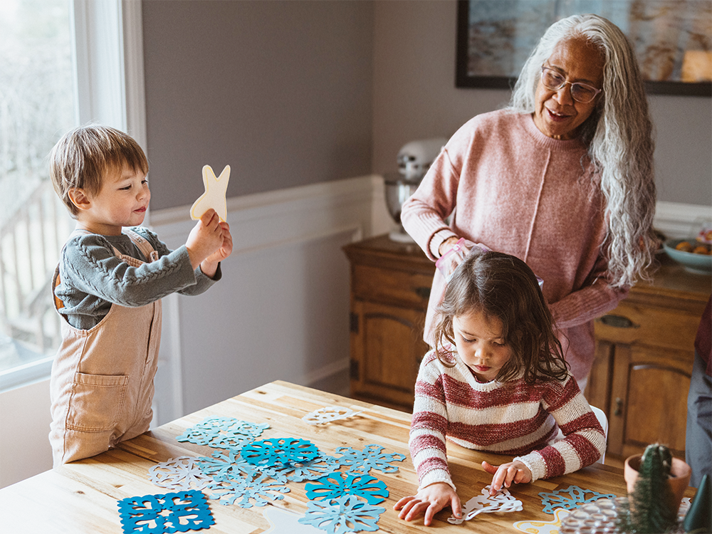 A grandma making paper snowflakes with her two grandchildren.