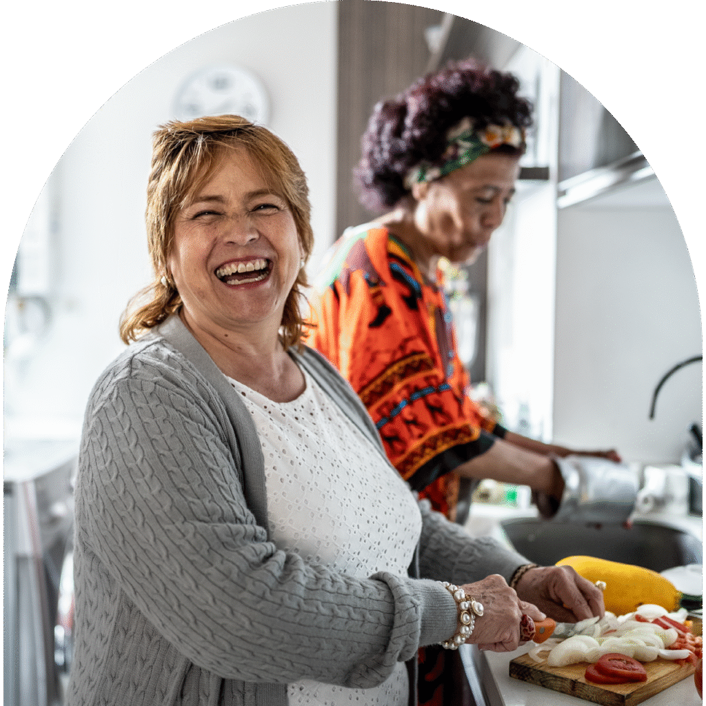 Two women making dinner together in the kitchen laughing.